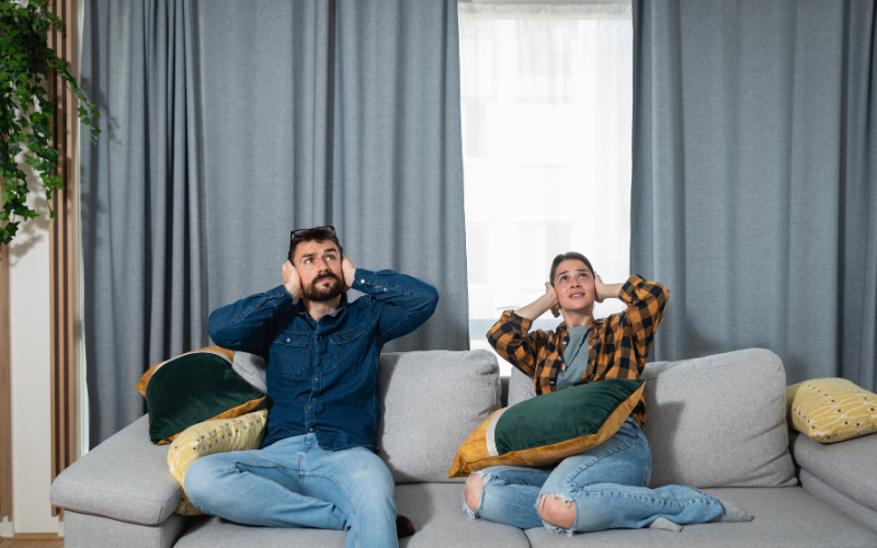 Hausordnung Ein Mann und eine Frau sitzen auf dem Sofa und halten sich die Ohren zu